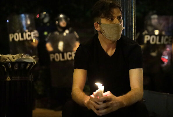 A man holds candle as he sits in front of a police perimeter near the White House.