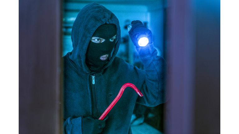 masked burglar with crowbar breaking and entering into a victim's home