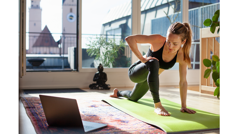 Woman exercising at home in front of her laptop, stretching her legs