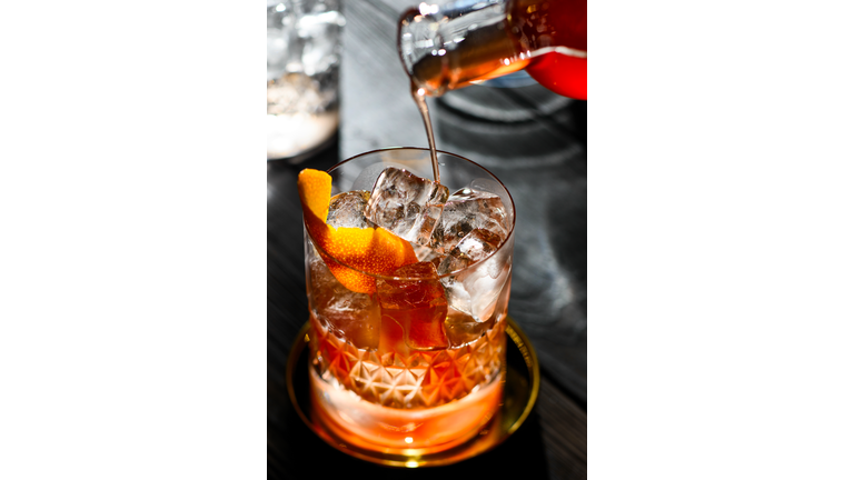 Pouring whiskey cocktail with orange peel