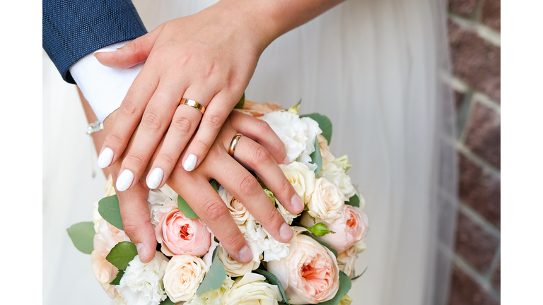 Hands of the bride and groom on the wedding bouquet.