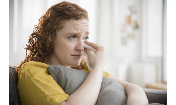 Crying Caucasian woman clutching pillow wiping tears