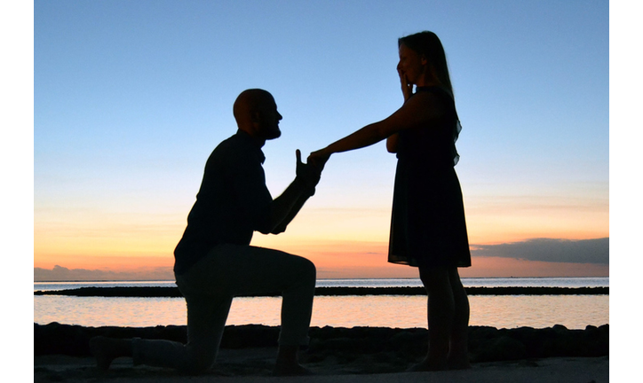 Silhouette Man Proposing Woman While Holding Hand At Beach Against Sky During Sunset