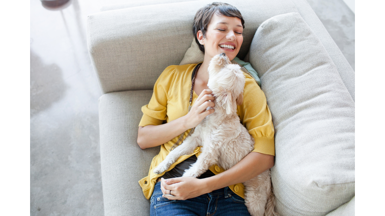 Young woman hugging dog on living room sofa