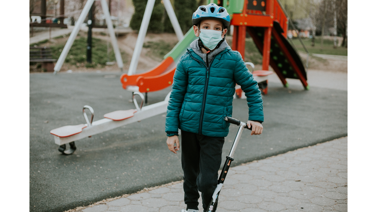 Young boy is standing on the empty playground while wearing face mask