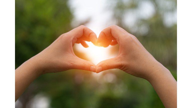 Female hands in the form of heart against the sky pass sun beams. Hands in shape of love heart