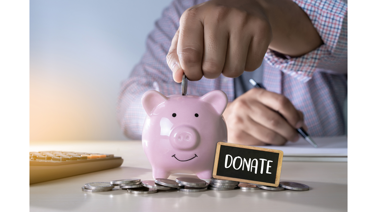 Midsection Of Businessman Inserting Coin In Piggy Bank For Charitable Donation