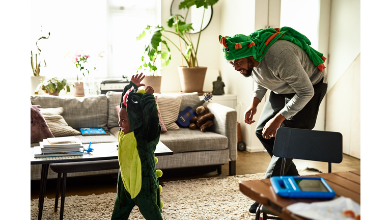 Father and son dressed as dragons playing in living room