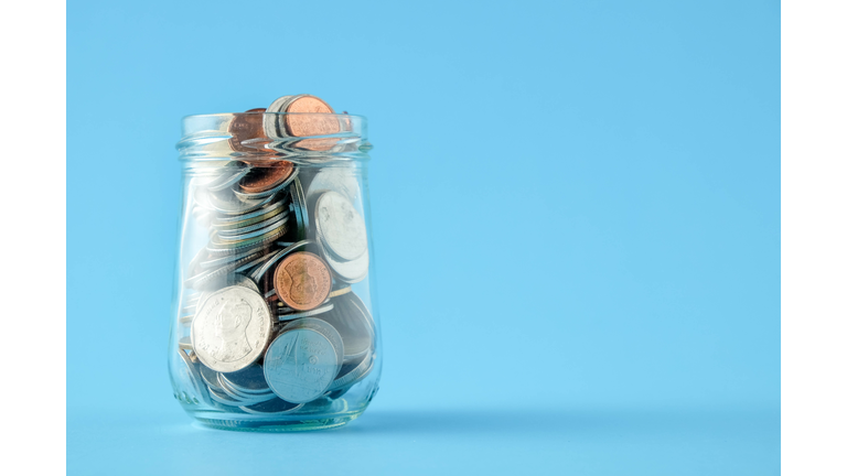 Close-Up Of Coins In Glass Jar On Blue Background