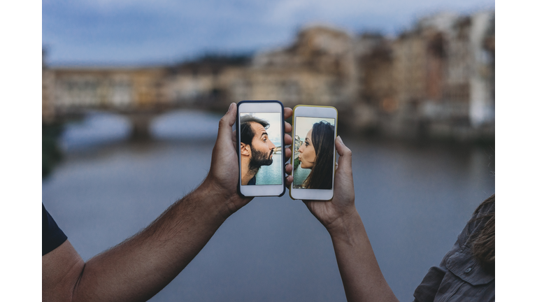 Conceptual shot of a young adult couple kissing via mobile phone