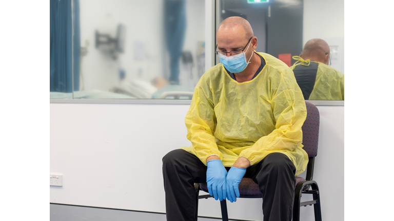 Male Health care sitting in a chair beside a closed hospital room looking exhausted