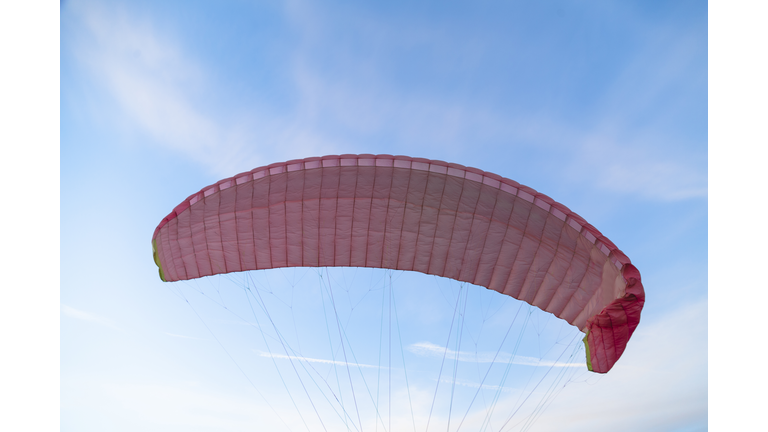 Pink dome of paraglider flying in blue bright sky