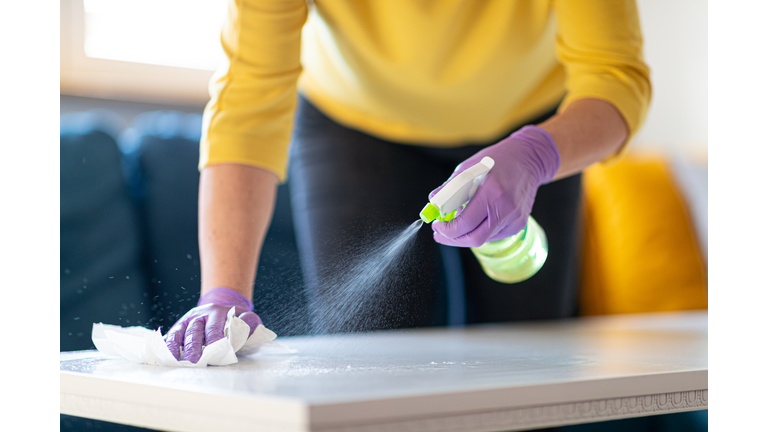 Hands in gloves disinfecting coffee table (GettyImages)