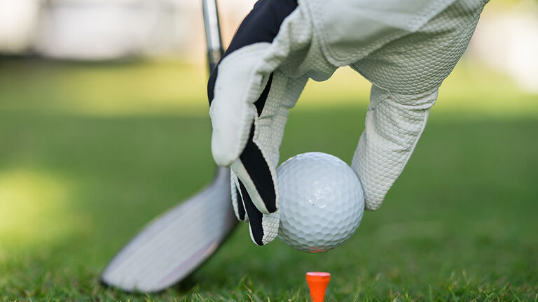 Hand putting golf ball on tee in golf course