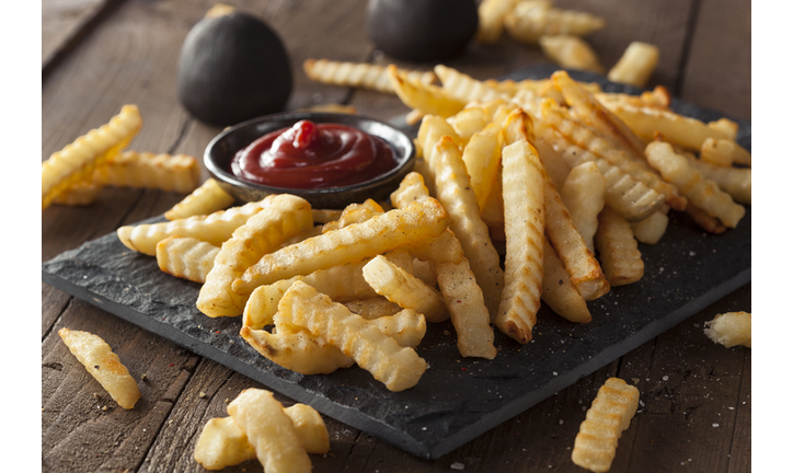 A plate of unhealthy baked crinkle French fries and ketchup