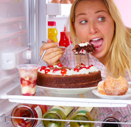 Young woman eating chocolate cake inside fridge