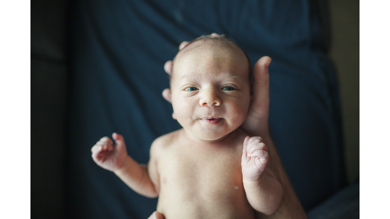 Overhead portrait of newborn baby boy held by father in hospital