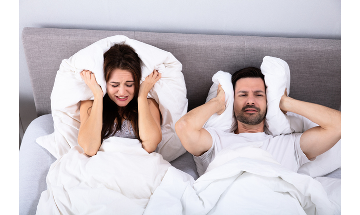 Couple Covering Their Ears With Pillow On Bed