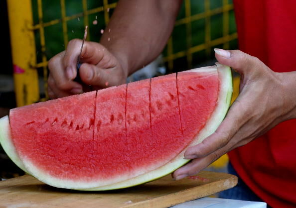 A vendor slices watermellon as he sells