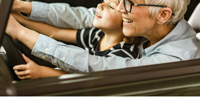 Happy grandmother and grandson testing new car in a showroom.