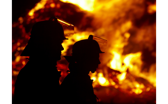 Silhouette of firefighters against large fire in the dark