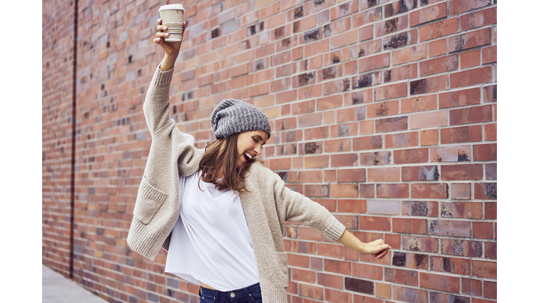 Happy woman with coffee to go singing and dancing on the street