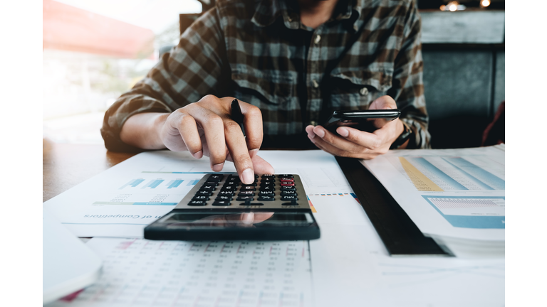 Midsection Of Businessman Using Mobile Phone And Calculator At Desk In Office