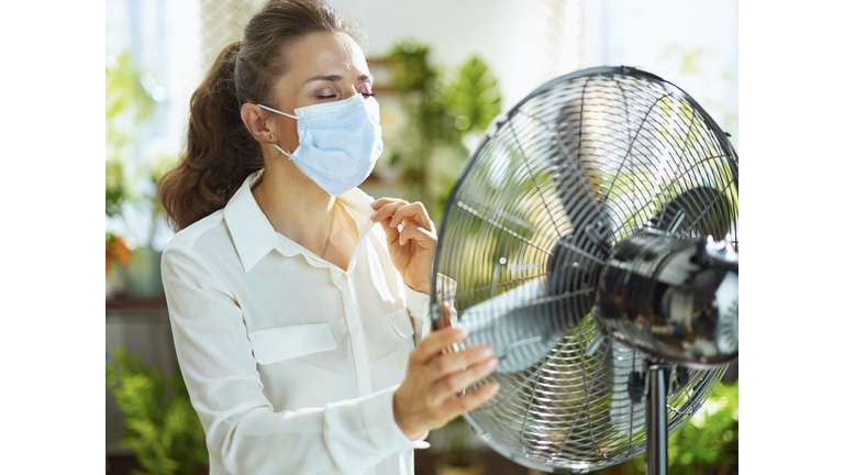 sad young female with electric fan feeling summer heat