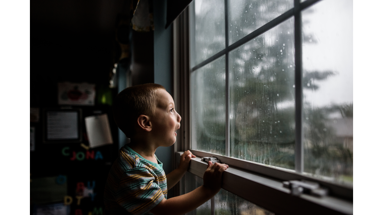 excited boy looking out a window with raindrops at a stormy sky