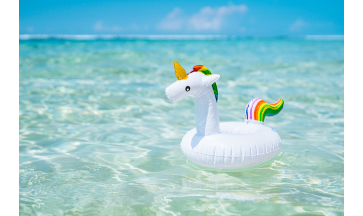 Inflatable white unicorn floating at transparent turquoise sea. Blue sky with few clouds on the background.