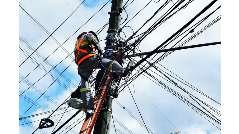 Low Angle View Of Electrician Working On Pole Against Cloudy Sky
