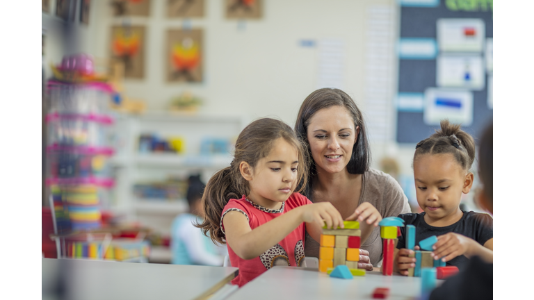 Pre-school teacher playing with girls in kindergarten