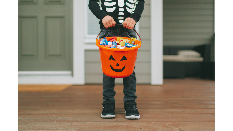Low Section Of Boy With Sweet Food In Bucket Standing At Home During Halloween