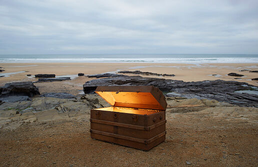 Open treasure chest of gold on a deserted beach.