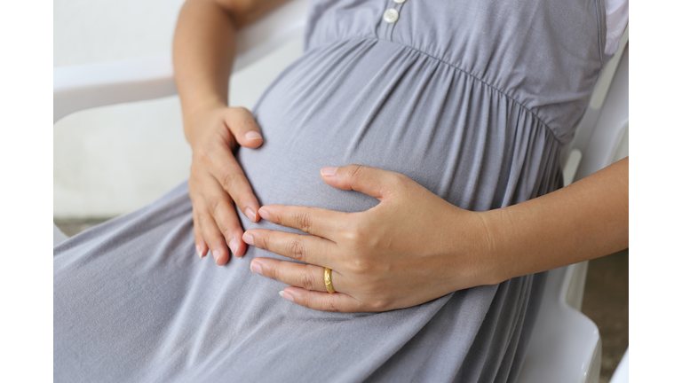 Midsection Of Pregnant Woman Sitting On Chair Against Wall