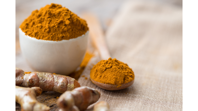 Turmeric powder and fresh turmeric in wood bowls on wooden table.