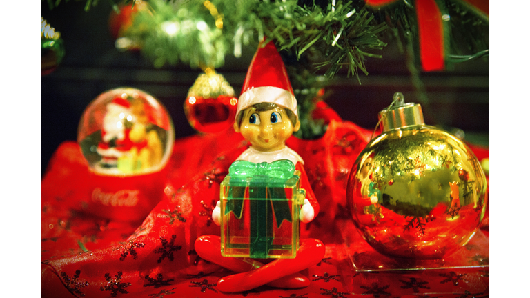 Christmas elf character holding a present under a Christmas tree