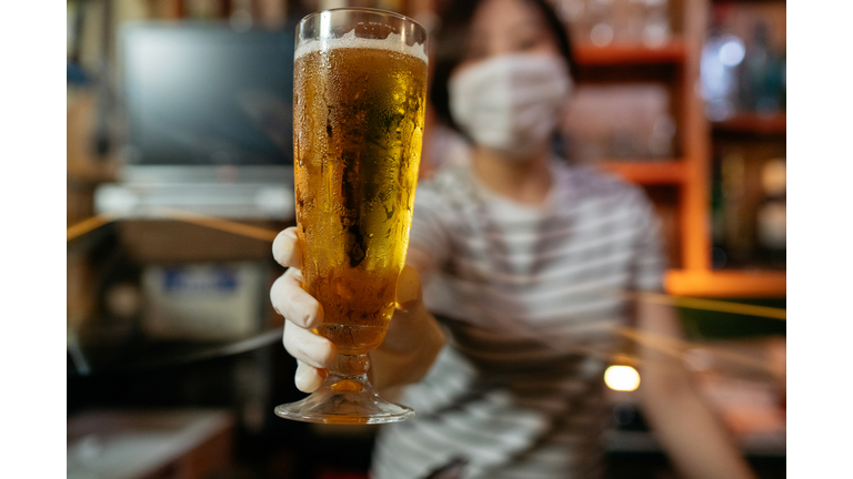 Bar owner serving beer with protective plastic glove from behind protective plastic curtain