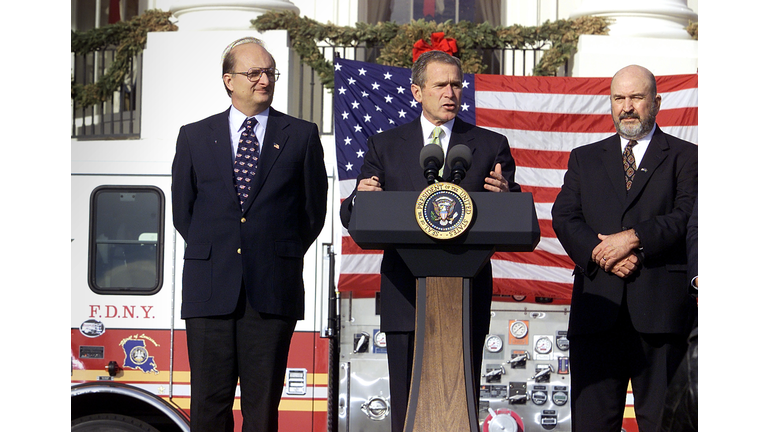 U.S. President George W. Bush (C), Ronald Goldman (L), and Governor Mike Foster (R) from Louisiana speak in front of fire truck on the South Lawn of the White House 19 December 2001 in Washington. (Photo: Stephen Jaffe/AFP via Getty Images)