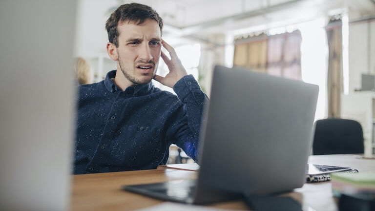 Confused businessman looking at laptop while sitting at desk in office