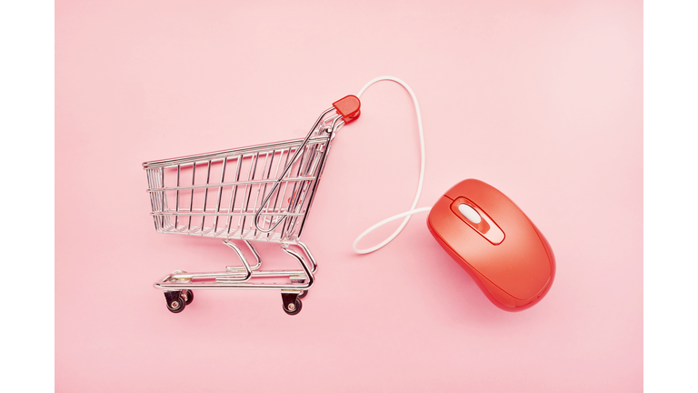 Still life of a small shopping cart and red computer mouse on pink background, online shopping