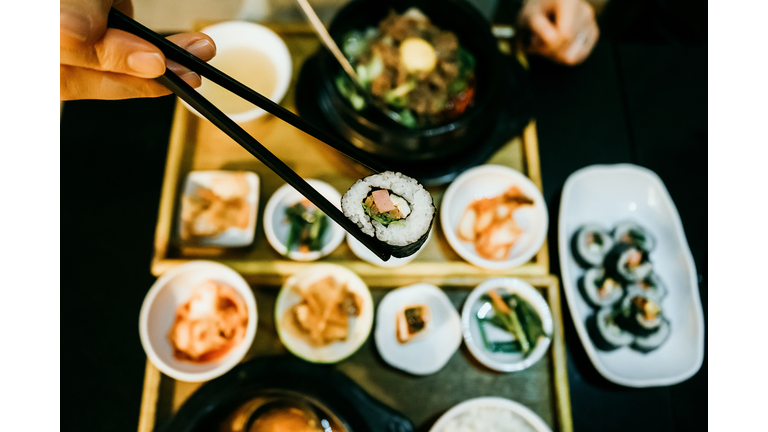 Overhead view of woman's hand eating kim bap with chopsticks against fresh Korean meal in restaurant