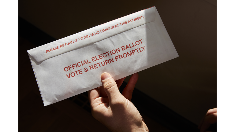 A person standing inside his home holding his mail in voting ballot