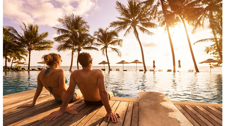 Couple enjoying beach vacation holidays at tropical resort with swimming pool and coconut palm trees near the coast with beautiful landscape at sunset, honeymoon destination