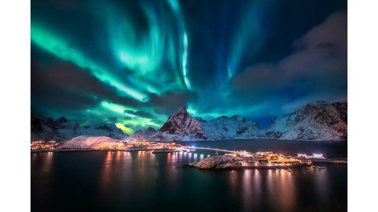 Aurora borealis. Lofoten islands, Norway. Aurora. Green northern lights. Starry sky with polar lights. Night winter landscape with aurora, sea with sky reflection and snowy mountains.