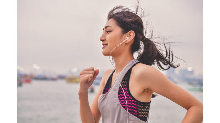 Woman Listening Music While Jogging By River Against Sky