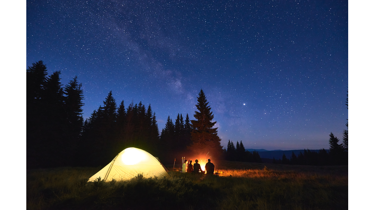 Tourists sitting near campfire under starry sky.