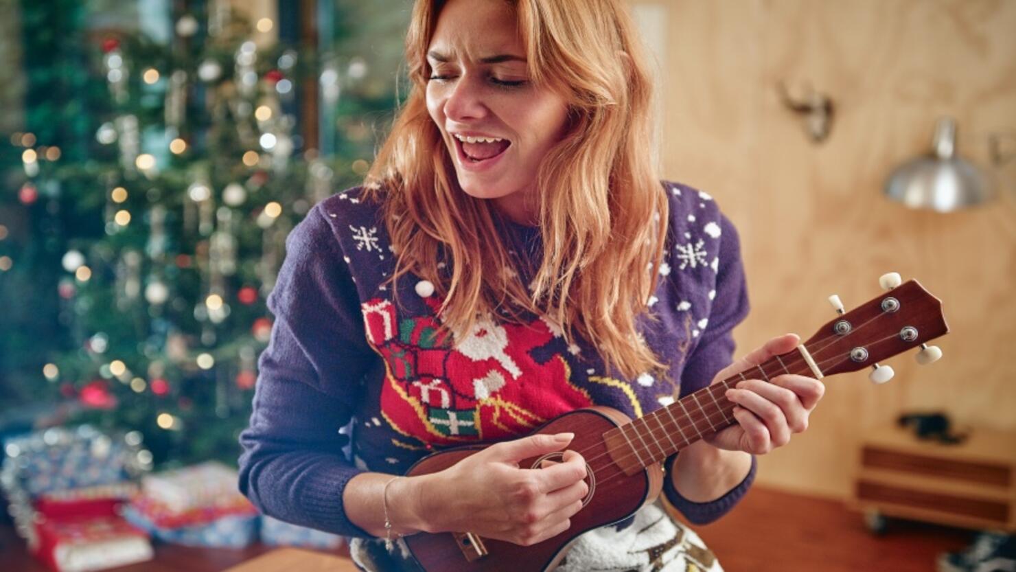 Blond woman playing ukulele in front of Christmas tree