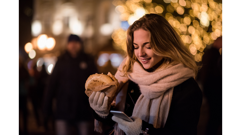 Smiling woman holding burger and using smartphone