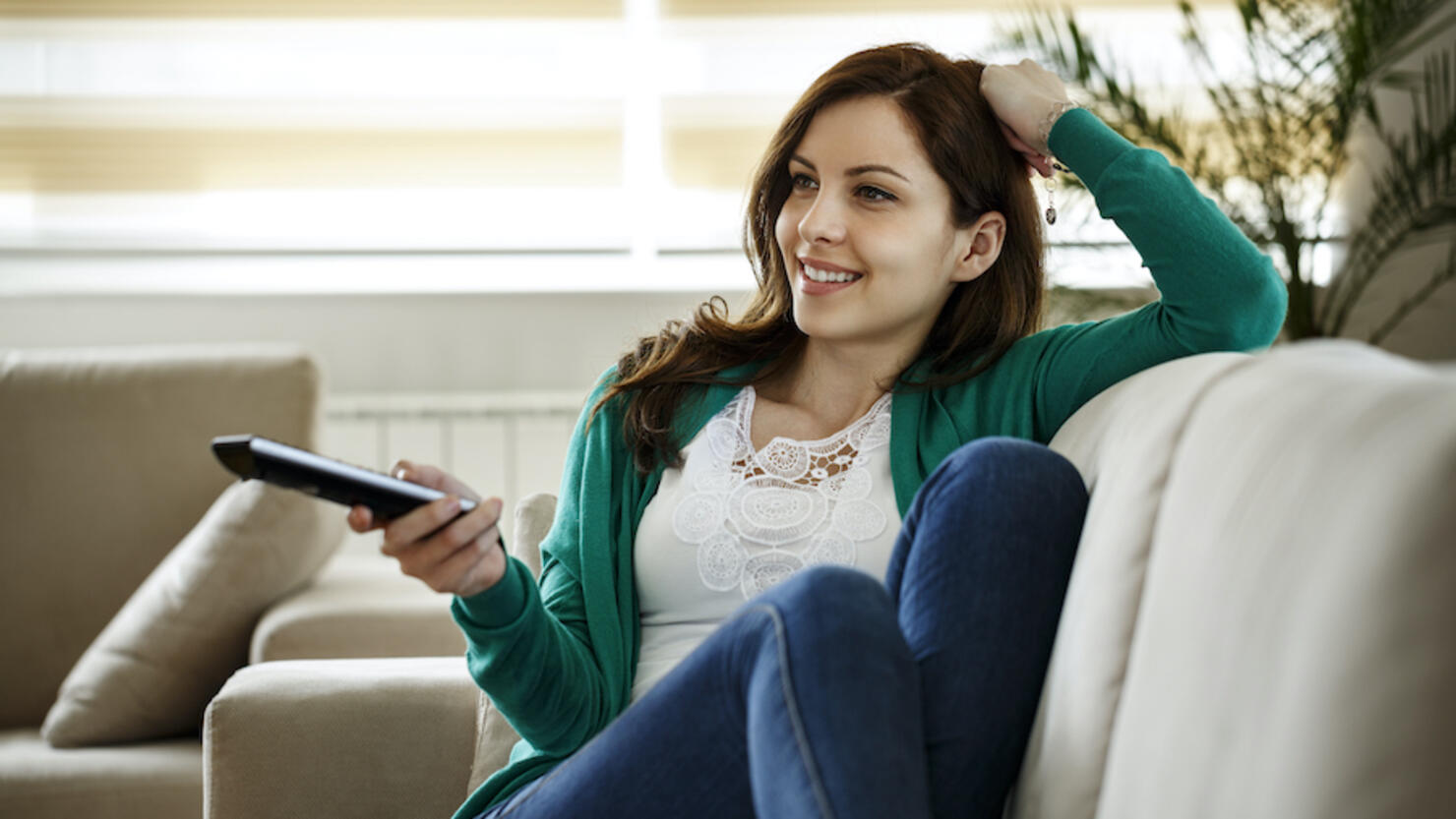 Smiling young woman watching TV during COVID-19 pandemic